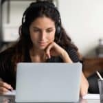 Focused female adult in headphones using laptop, using HR Service Delivery on internet